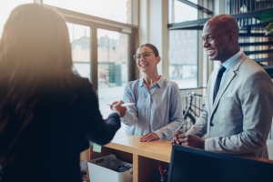 Two Smiling Hotel Guests Giving Their Reservation Documents to Reception